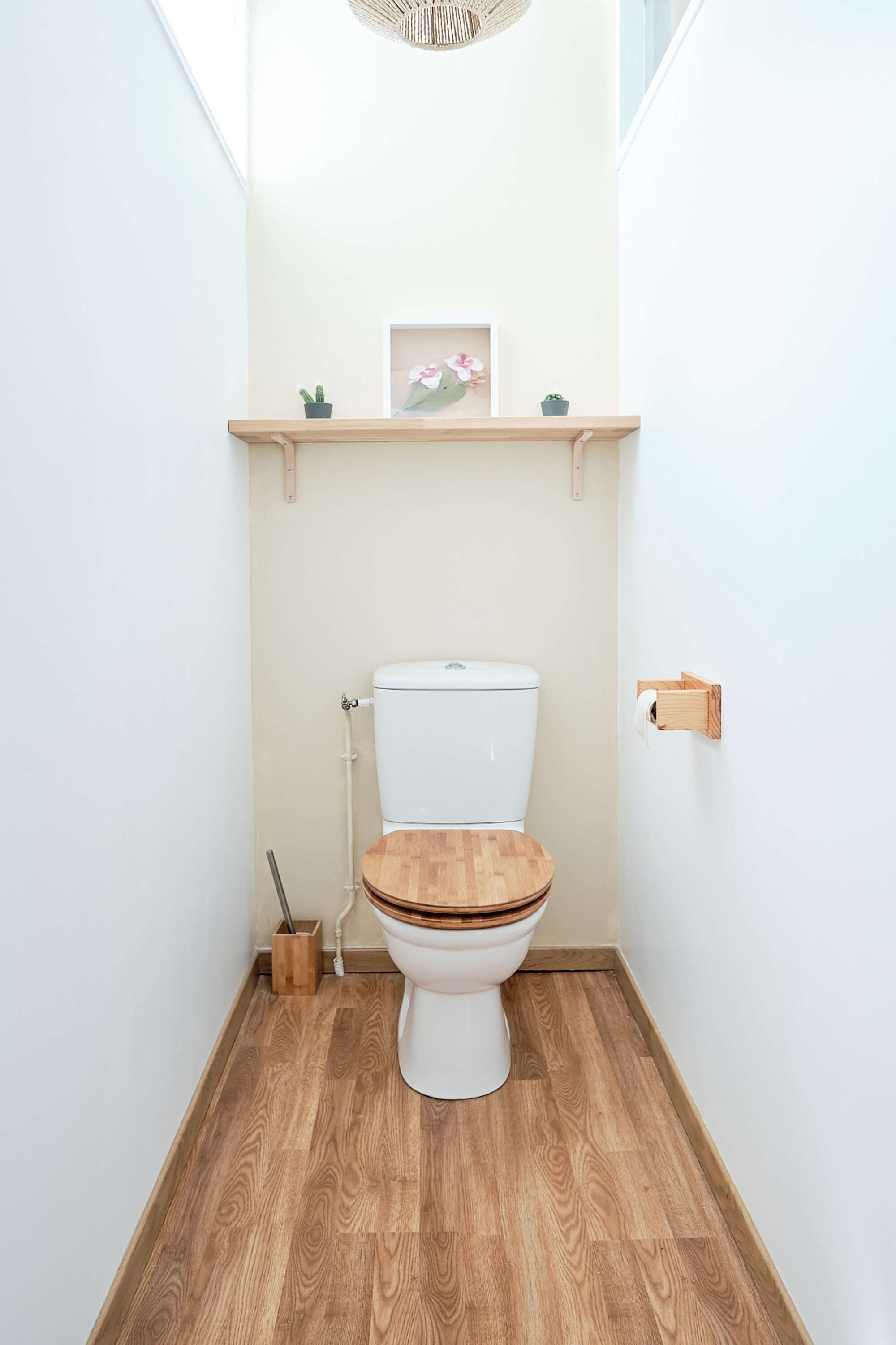Ein kleines, modernes Badezimmer mit Holzboden, Toilette in Weiß und einem Holzregal darüber.