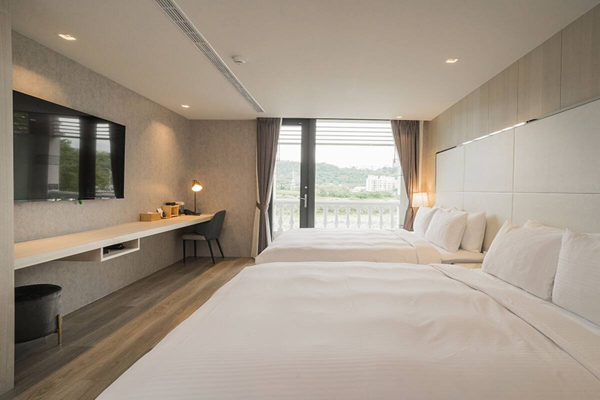 Habitación de hotel con dos camas, un escritorio, una silla, un espejo grande y un balcón con vistas.
