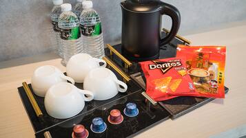 A tray with white teapots, a black coffee pot, bottled water, and a bag of Doritos chips.