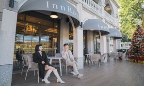 An outdoor seating area of an InnRosa hotel with a modern architectural design, featuring large windows and a Christmas tree decoration. - Roselnn (Taoyuan City)