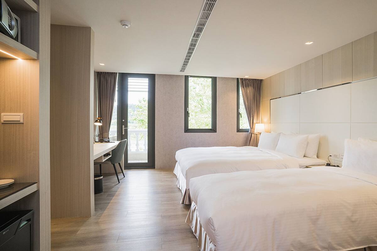 Habitación de hotel con dos camas, un escritorio y vistas a zonas verdes.