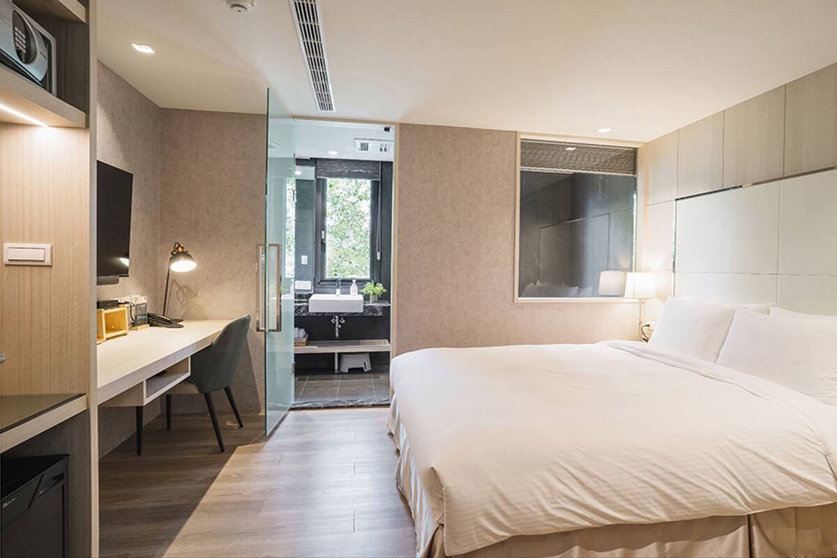 Una habitación de hotel moderna con una cama grande, un escritorio y un baño visible a través de una puerta abierta.