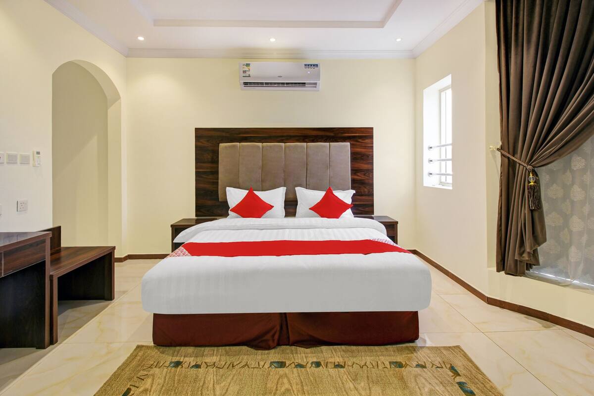 A hotel room with a large bed, a desk, and a window with curtains.