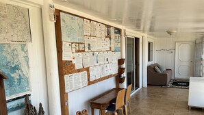Une pièce avec un panneau d’affichage en bois recouvert de cartes et de documents, une table en bois avec des chaises, un canapé et un tapis à motifs.