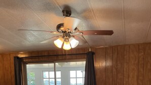 Un coin repas avec une table et des chaises en bois, un ventilateur de plafond et une vue sur l’extérieur à travers des portes vitrées.