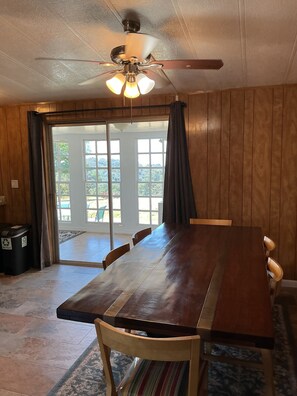 A dining area with a wooden table and chairs, a ceiling fan, and a view through glass doors to the outside.