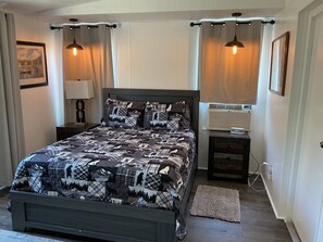 A bedroom with a bed, bedside tables, a lamp, an air conditioner, and a rug.