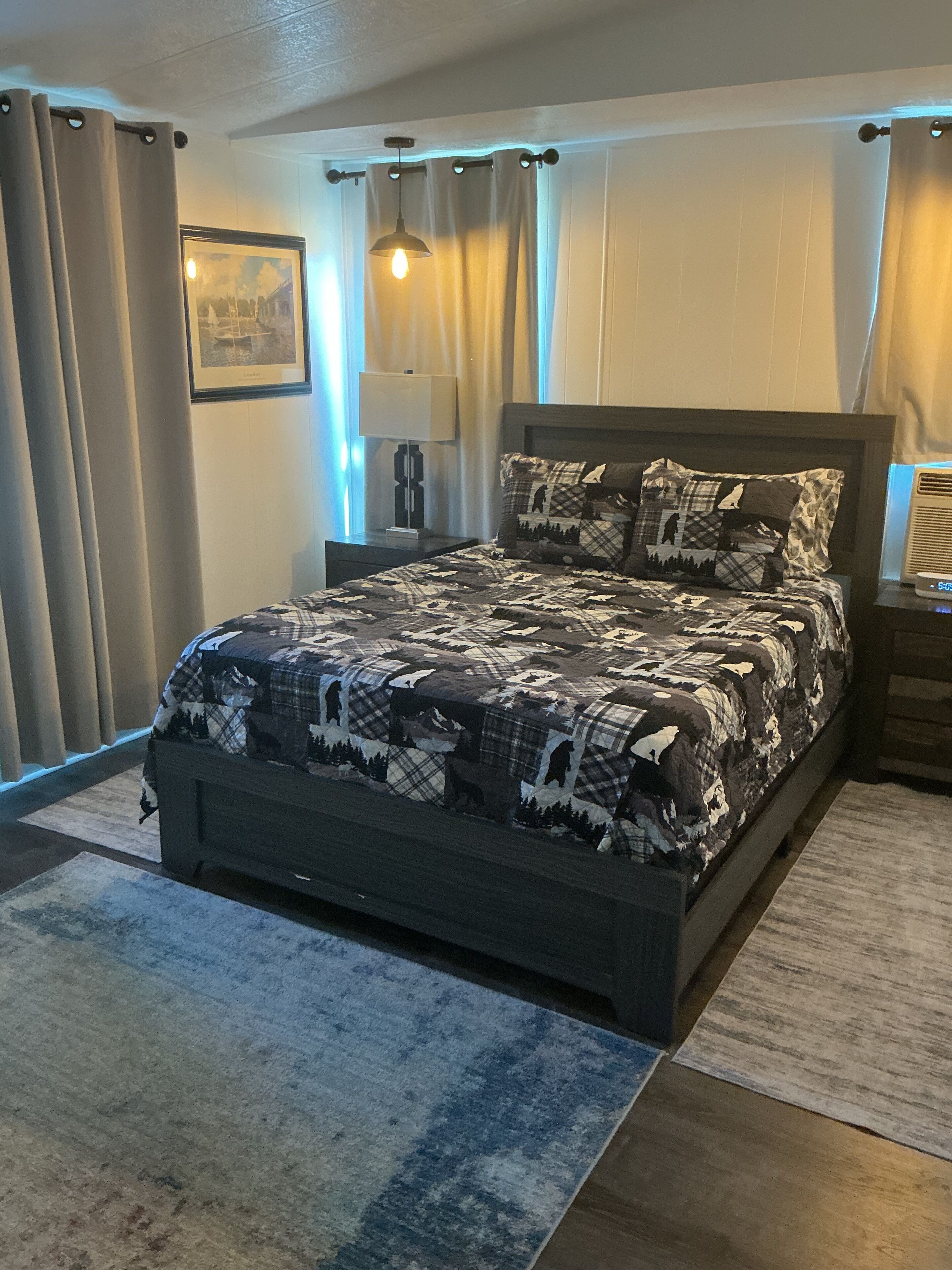 A bedroom with a bed, curtains, a lamp, a picture frame, and a heater.