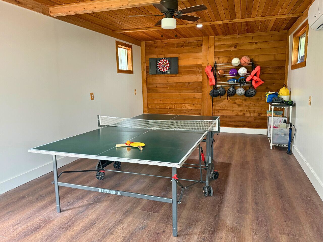 A ping pong table in a room with wooden walls and a ceiling fan.