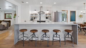 A modern kitchen with a central island, bar stools, and a dining area with a chandelier.