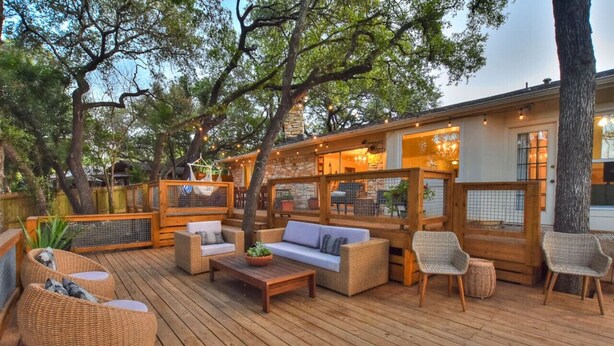 An outdoor deck with wicker furniture, a wooden table, and a stone fireplace.