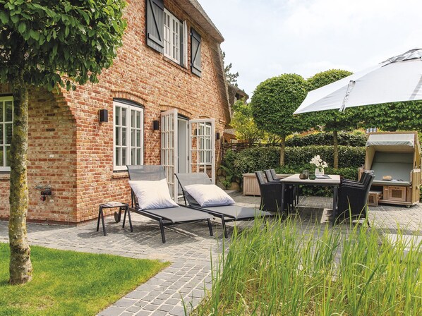 A brick building with a patio area featuring lounge chairs, a table, and an umbrella.