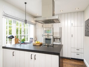 A modern kitchen with white cabinetry, a black countertop, stainless steel appliances, and a large window providing natural light.