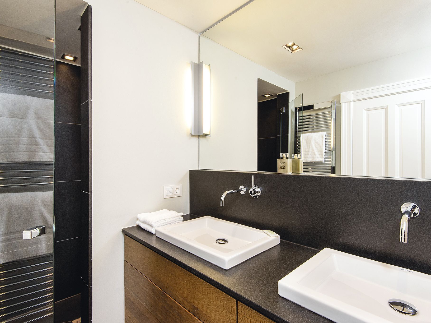 A modern bathroom with two sinks, a large mirror, and a towel rack.