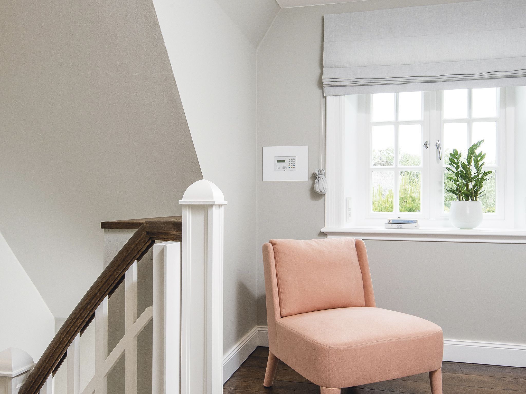 A staircase with white railings and a wooden handrail, leading to a room with a window, a thermostat, and a potted plant.