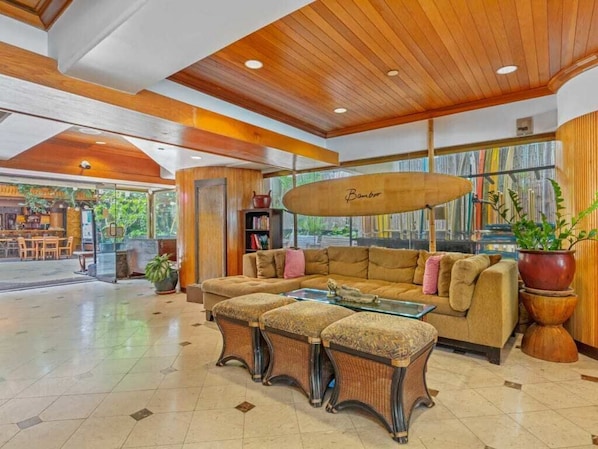 A spacious lobby with a wooden ceiling, a large sofa, a glass coffee table, and a bookshelf.