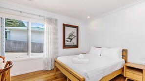 Une chambre à coucher avec un lit en bois, une table de chevet, une fenêtre avec des rideaux et un tableau encadré au mur.