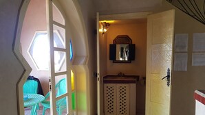 A hallway with a door leading to a bathroom, a window with a view, and a green chair outside.