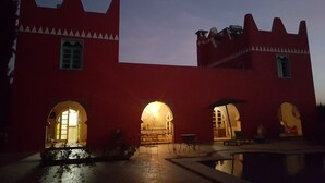 A building with a red facade and arched windows, featuring a courtyard with a pool and outdoor seating.