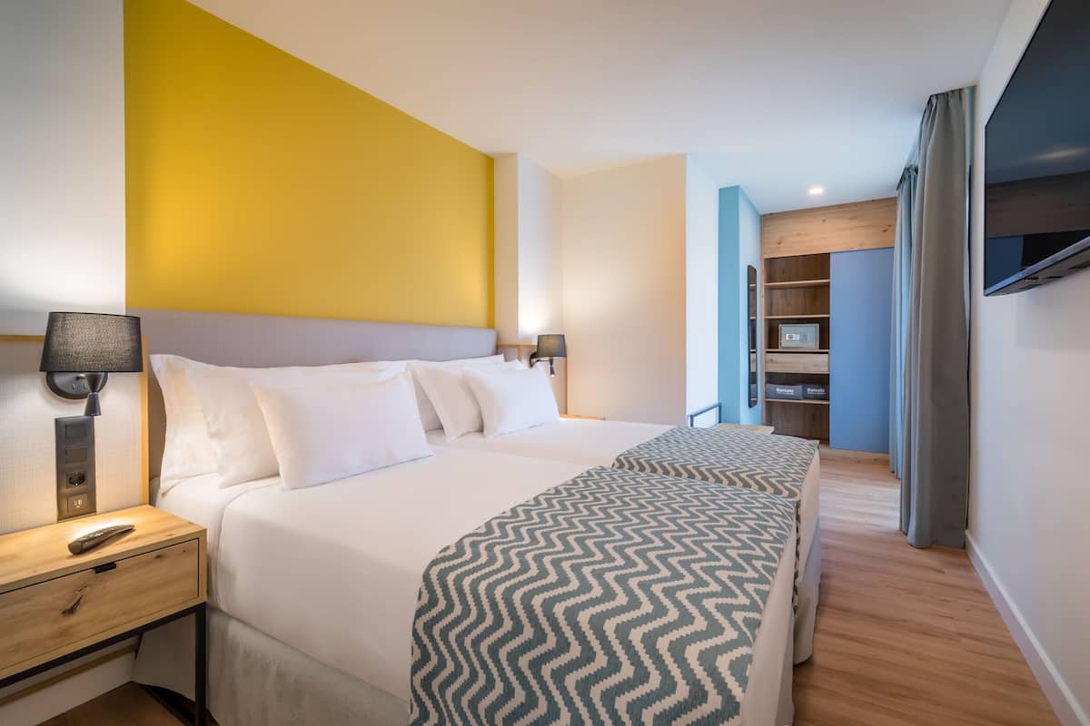 A hotel room with a large bed, bedside lamps, a TV, and a wardrobe.
