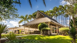 A resort with a thatched roof pavilion, palm trees, and a well-maintained lawn.