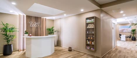 Zona de recepción con un mostrador de madera, plantas en macetas y una estantería con productos.