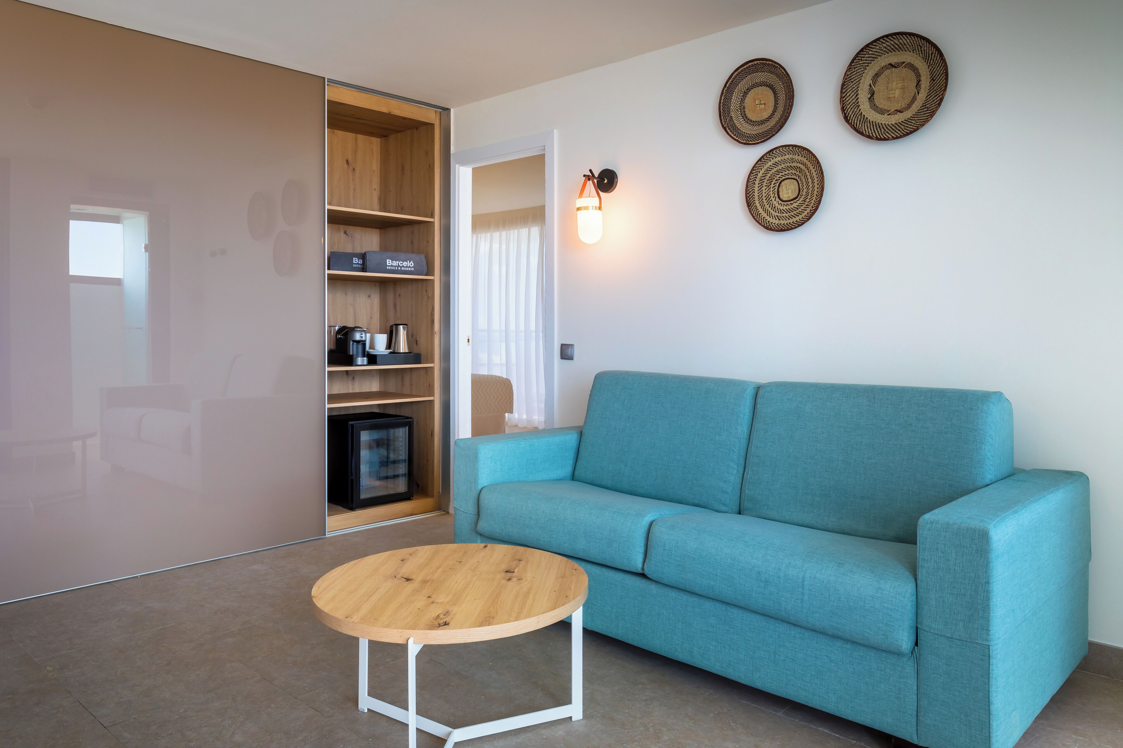 A modern living room with a teal sofa, a wooden coffee table, and a built-in shelving unit with a coffee maker and a small TV.