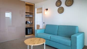 Una sala moderna con un sofá verde azulado, una mesa de centro de madera y una unidad de estanterías empotrada con una cafetera y un televisor pequeño.