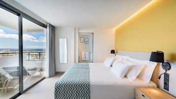 Ein modernes Hotelzimmer mit einem großen Bett, Nachttischen, einem Beistelltisch, einem Balkon mit Glastür und Blick auf die Stadtlandschaft.
