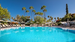 A clear blue pool with lounge chairs and umbrellas, surrounded by palm trees and other greenery.