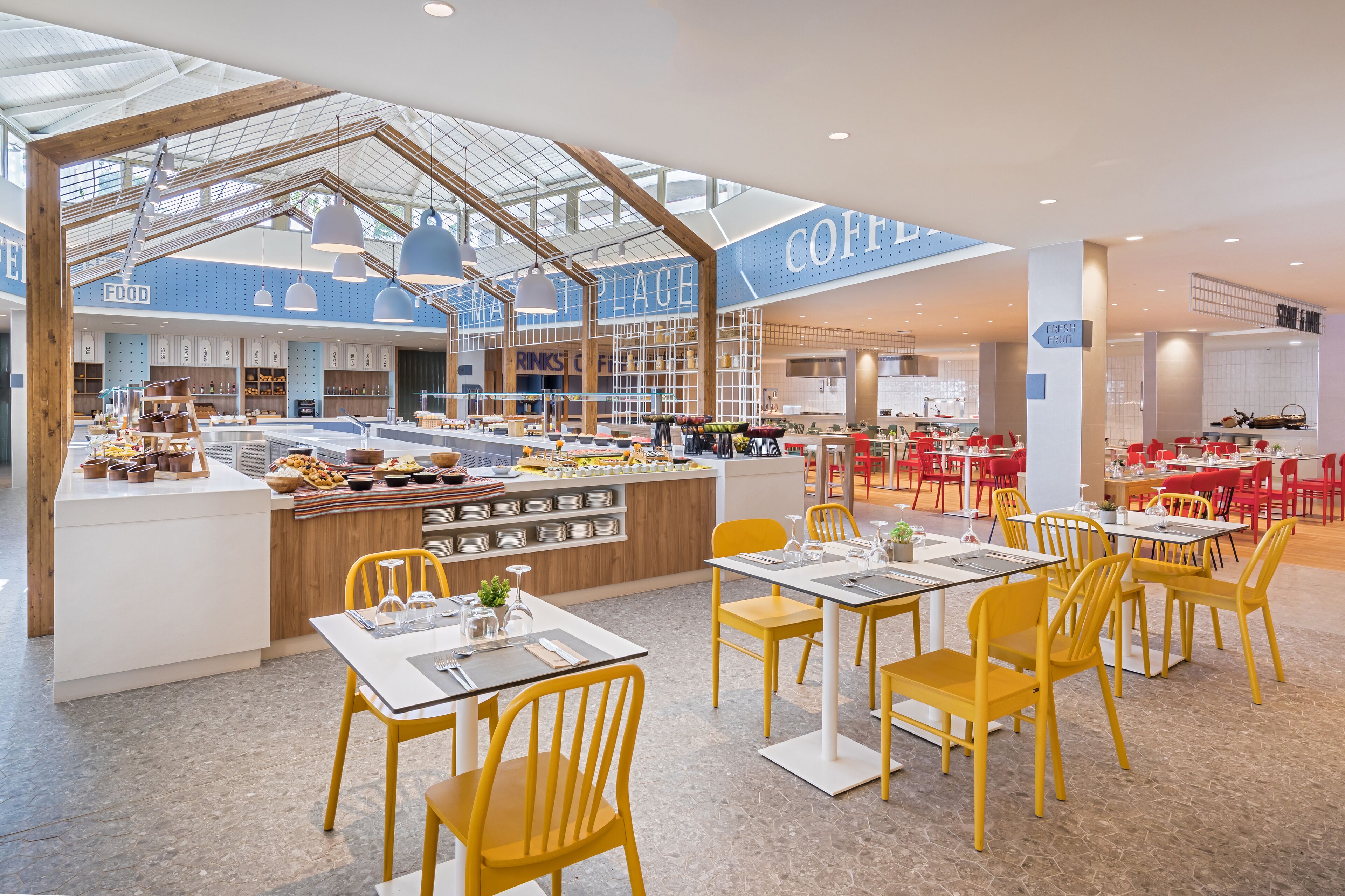 Un café moderno con mostrador central, sillas amarillas y mesas dispuestas a su alrededor.