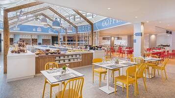 Un café moderno con mostrador central, sillas amarillas y mesas dispuestas a su alrededor.