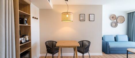 Una sala de estar moderna con una mesa de comedor de madera, dos sillas negras, un sofá azul y una máquina de café sobre una estantería de madera.