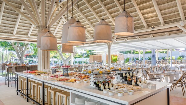 A buffet setup with various food items, bar stools, and hanging pendant lights.