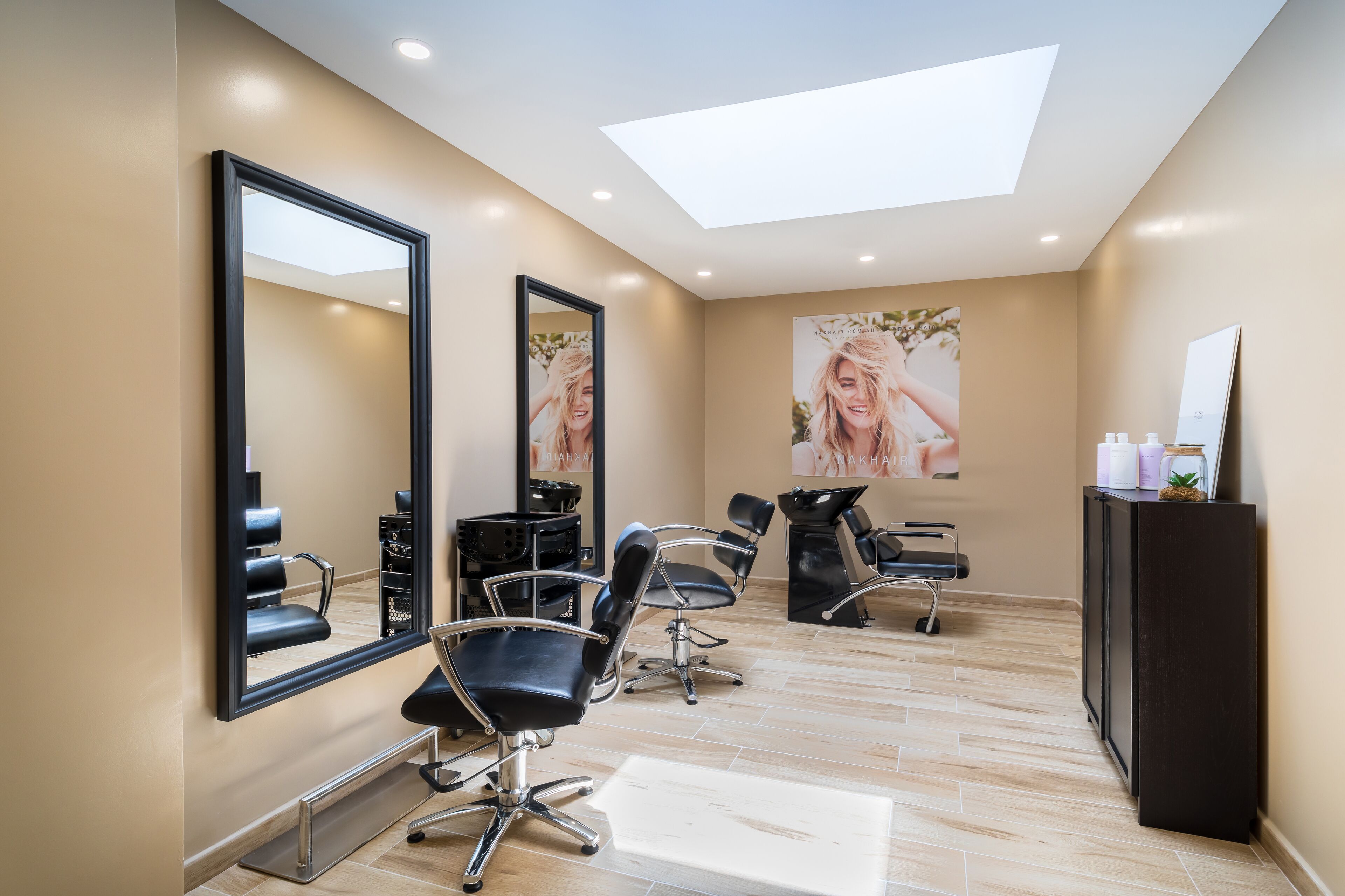 A hair salon with three black salon chairs, a large mirror, and a ceiling skylight.