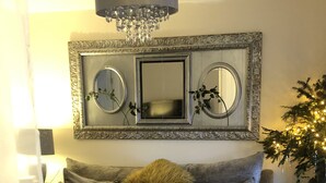 A living room with a grey sofa, decorative pillows, a chandelier, and two round mirrors framed in an ornate style. - Lazy Nest - Sleeps 4, Parking, Garden & Hammocks (Oakham)