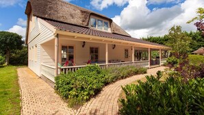 A house with a thatched roof, a covered porch, and a brick pathway leading to the entrance.