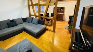 Een moderne woonkamer met een hoekbank, houten balken, een eethoek en een televisie.