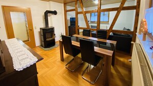 Een gezellige kamer met een houten tafel, stoelen, een open haard en een groot raam.