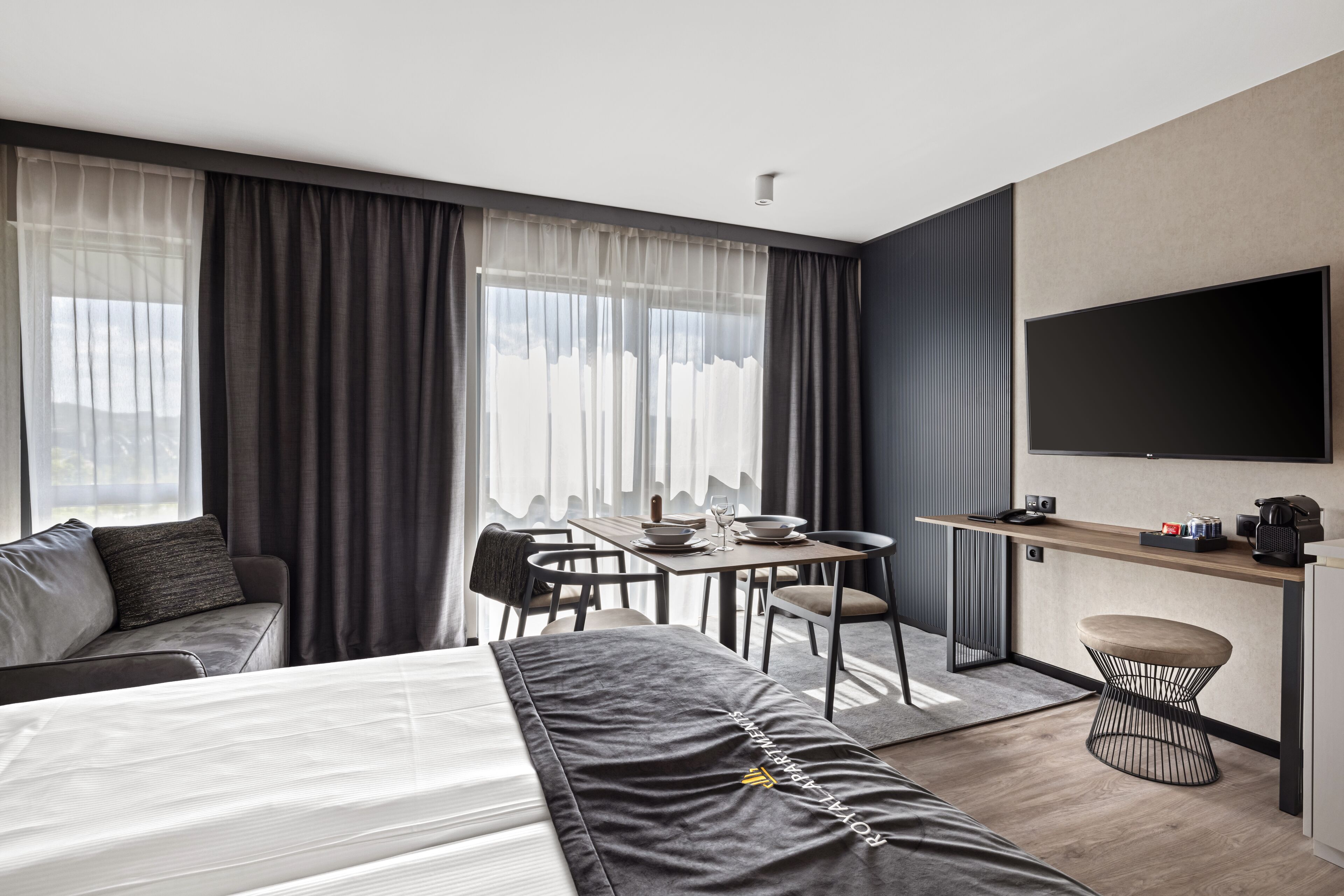 A modern hotel room with a bed, a desk, a dining table, and a TV.