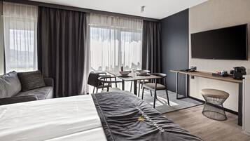 A modern hotel room with a bed, a desk, a dining table, and a TV.