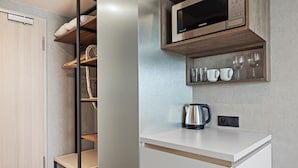 Une cuisine moderne équipée d’un four à micro-ondes encastré, d’une bouilloire et d’une étagère où sont rangées des tasses et des verres.