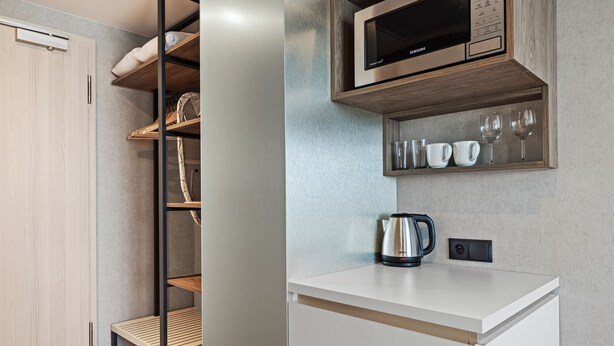 A modern kitchen with a built-in microwave, a kettle, and a shelf with cups and glasses.