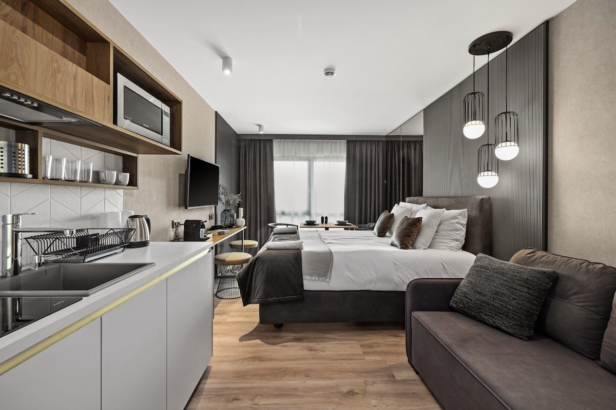 Een moderne hotelkamer met kitchenette, een groot bed met veel kussens, een bank en een eethoek met uitzicht.