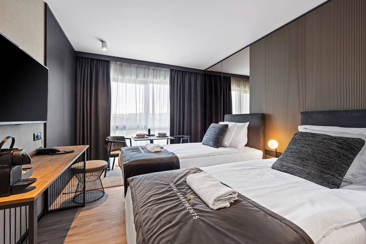 A hotel room with two beds, a desk, a chair, a TV, and a window with curtains.