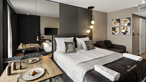 A modern hotel room with a large bed, a wooden dining table, and a flat-screen TV.