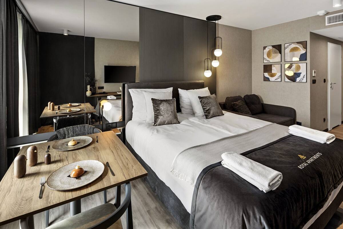 A modern hotel room with a large bed, a wooden dining table, and a flat-screen TV.