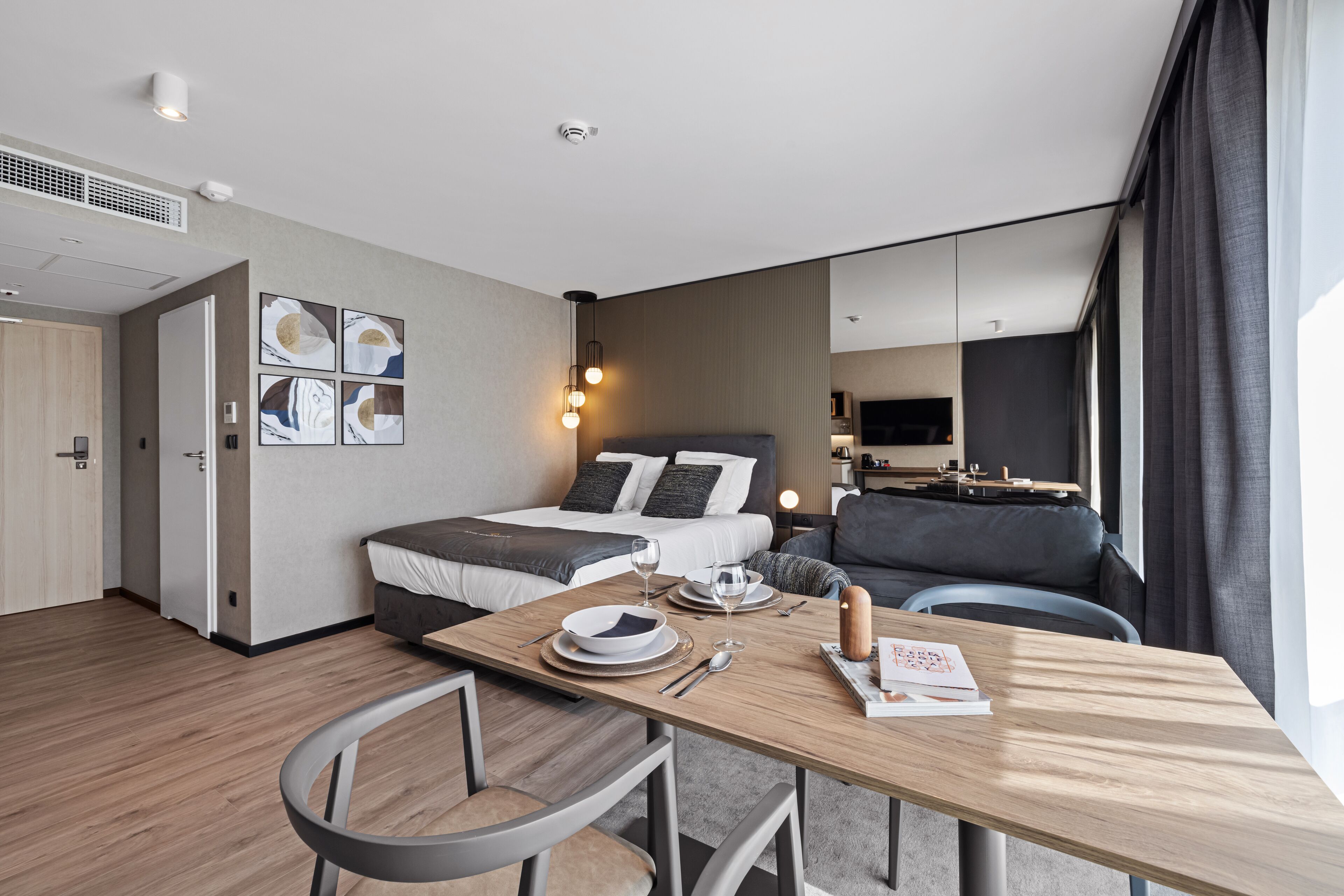 Une chambre d’hôtel moderne équipée d’un lit, d’une table à manger avec des chaises, d’un canapé et d’un téléviseur.