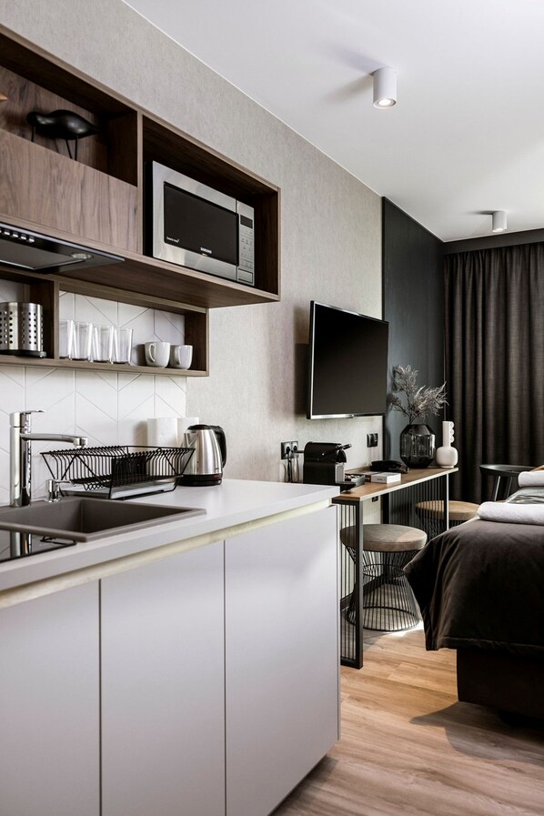Een moderne hotelkamer met een keukenhoek, een flatscreen televisie aan de muur en een bed met een donkere hoofdbord.