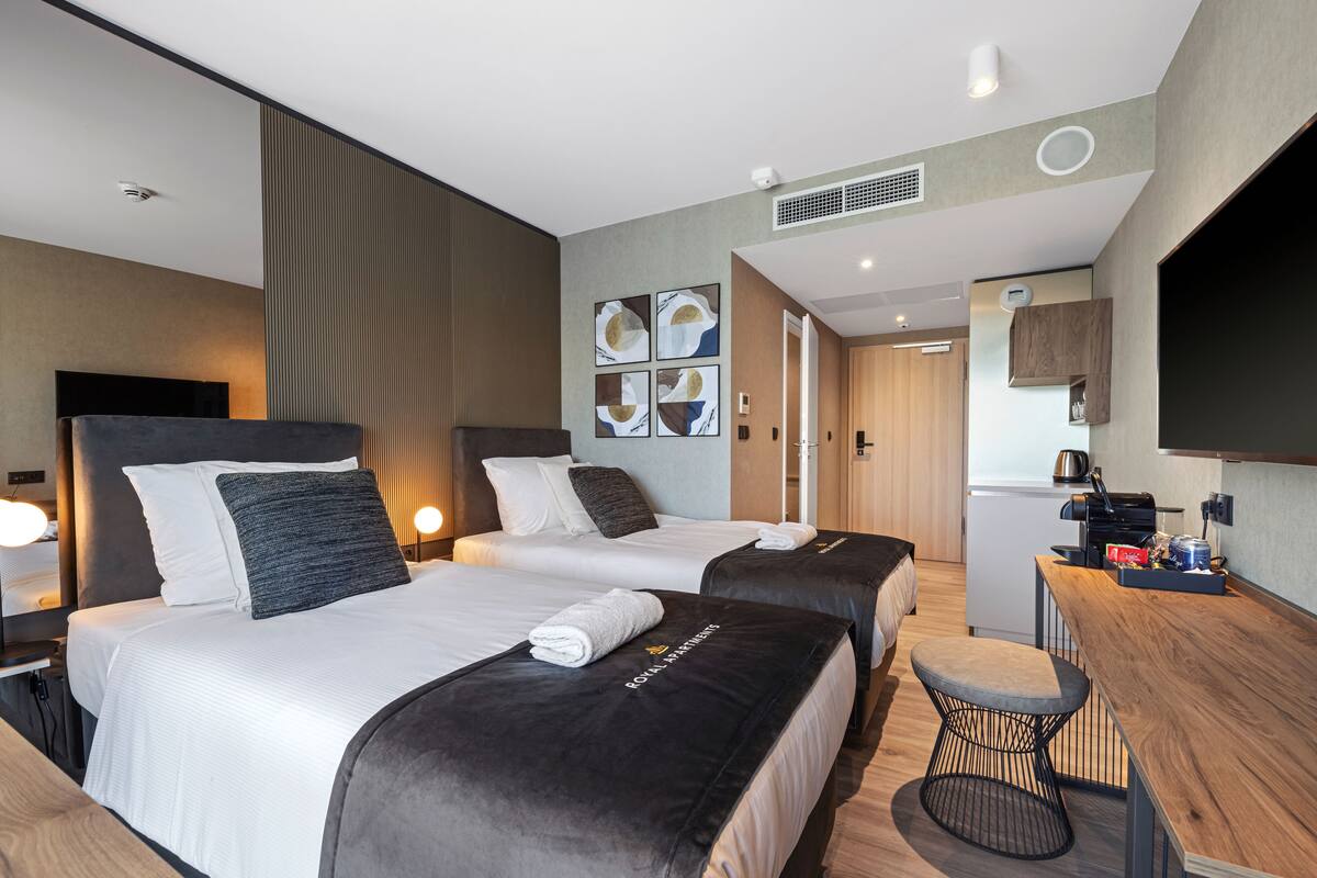 A hotel room with two beds, a desk, and a television.